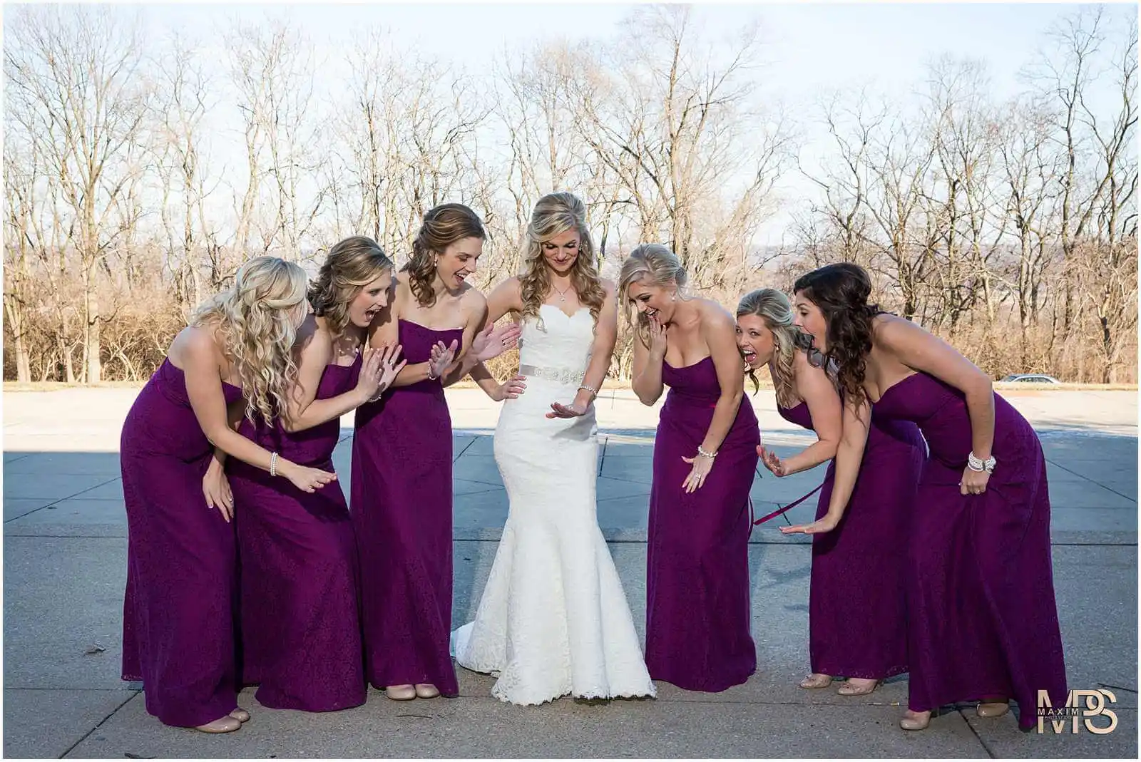 Bride and bridesmaids in purple gowns admiring wedding dress.