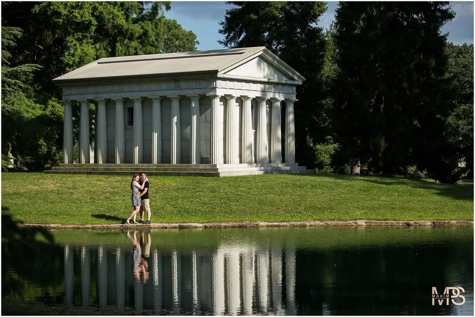 Romantic couple embracing by serene pond and classical building.