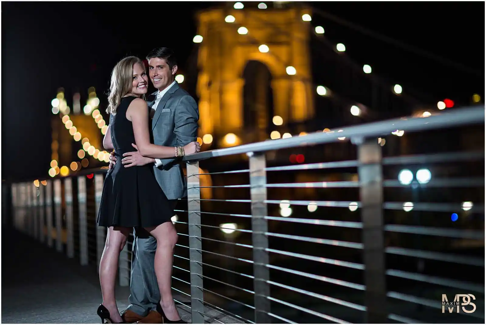Couple embracing on a bridge with Cincinnati lights at night.
