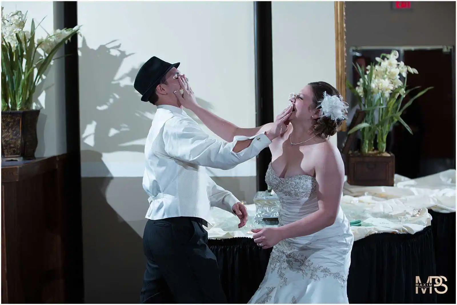 Bride and groom enjoying cake smashing at wedding reception.
