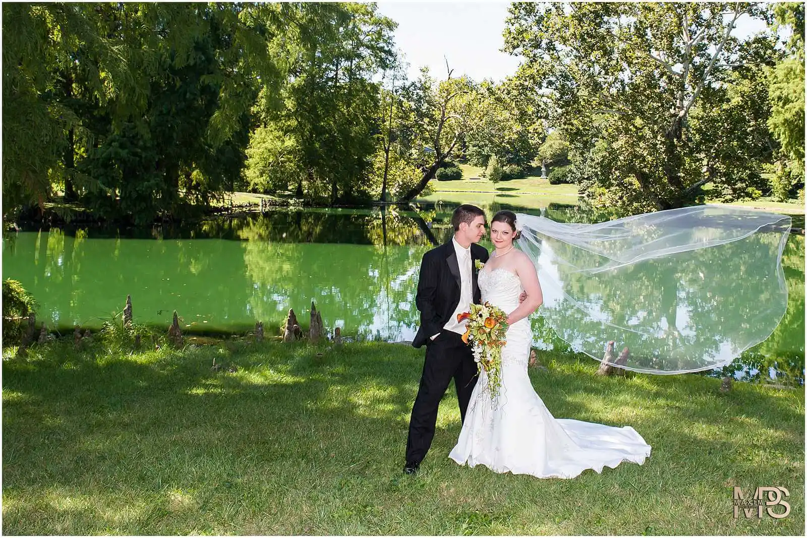 Bride and groom posing by a serene lakeside on wedding day.
