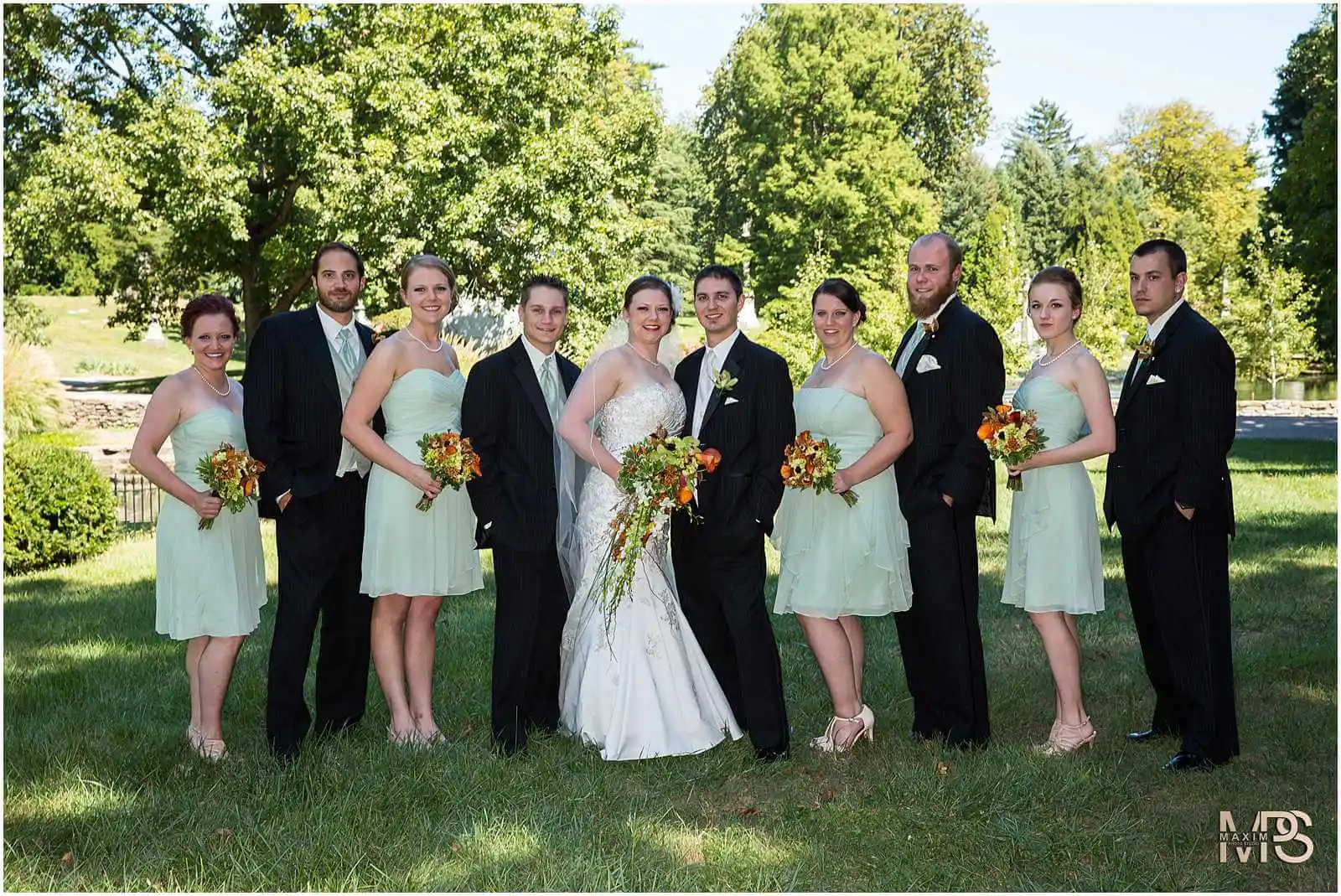 Outdoor wedding party posing in formal attire on a sunny day.