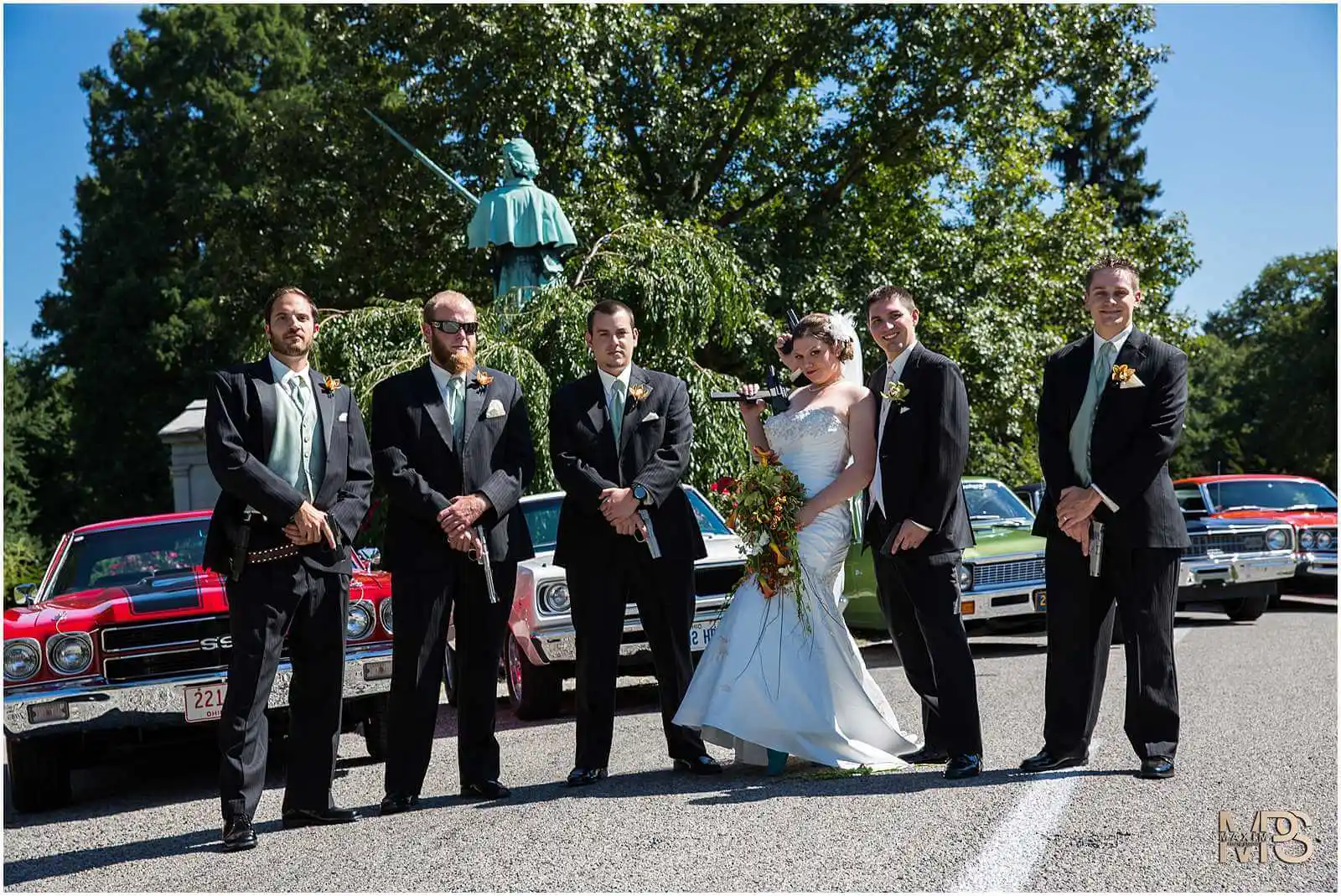 Outdoor wedding party with classic cars and stylish attire.