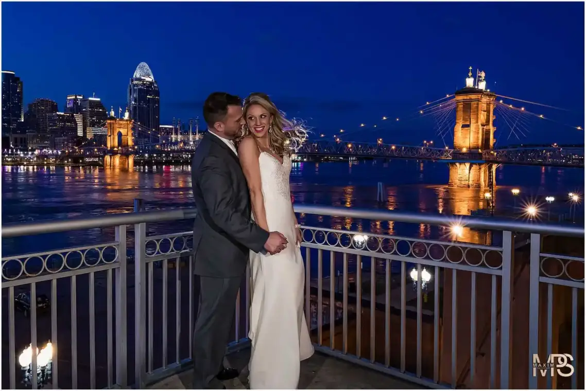 Romantic couple hugging by illuminated Roebling bridge at night Marriott Rivercenter Covington KY wedding.